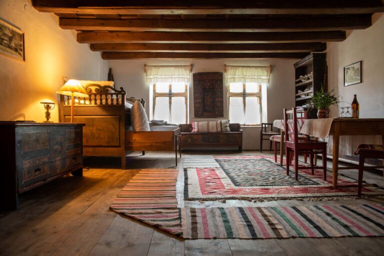 Rustikal eingerichtetes Zimmer mit Holzbalkendecke, antiken Möbeln und handgewebten Teppichen auf einem Holzboden.