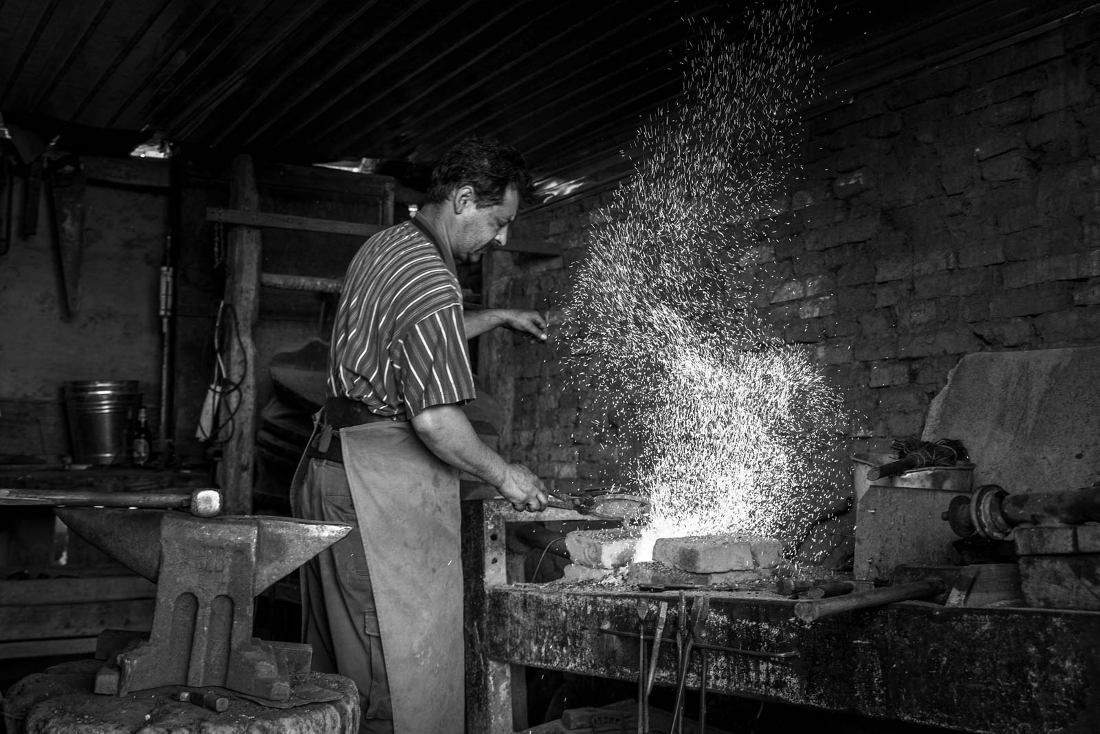Schmied arbeitet in einer Werkstatt an glühendem Metall, Funken sprühen hoch auf