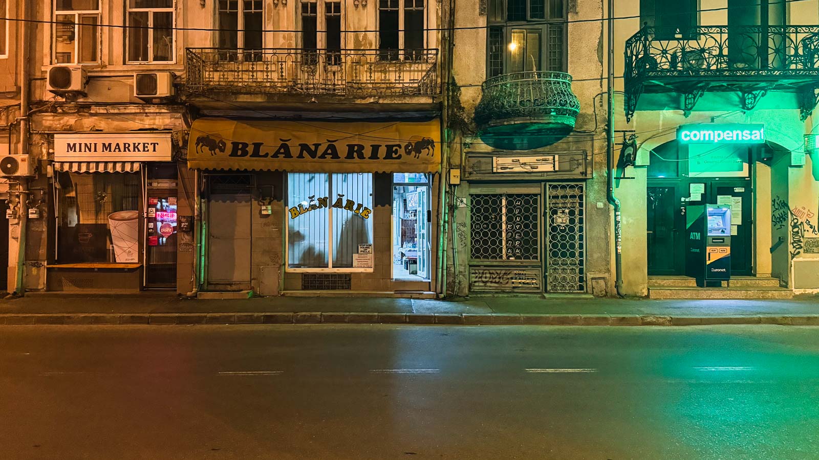 Nachtansicht einer Straße mit leeren Ladenfronten, darunter Mini Market, Blanarie und ein hellgrüner Geldautomat
