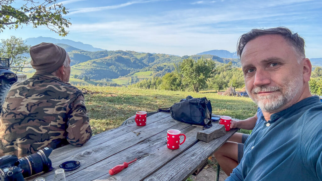 Zwei Männer sitzen an einem Picknicktisch mit roten Bechern und genießen die Aussicht auf grüne Berge